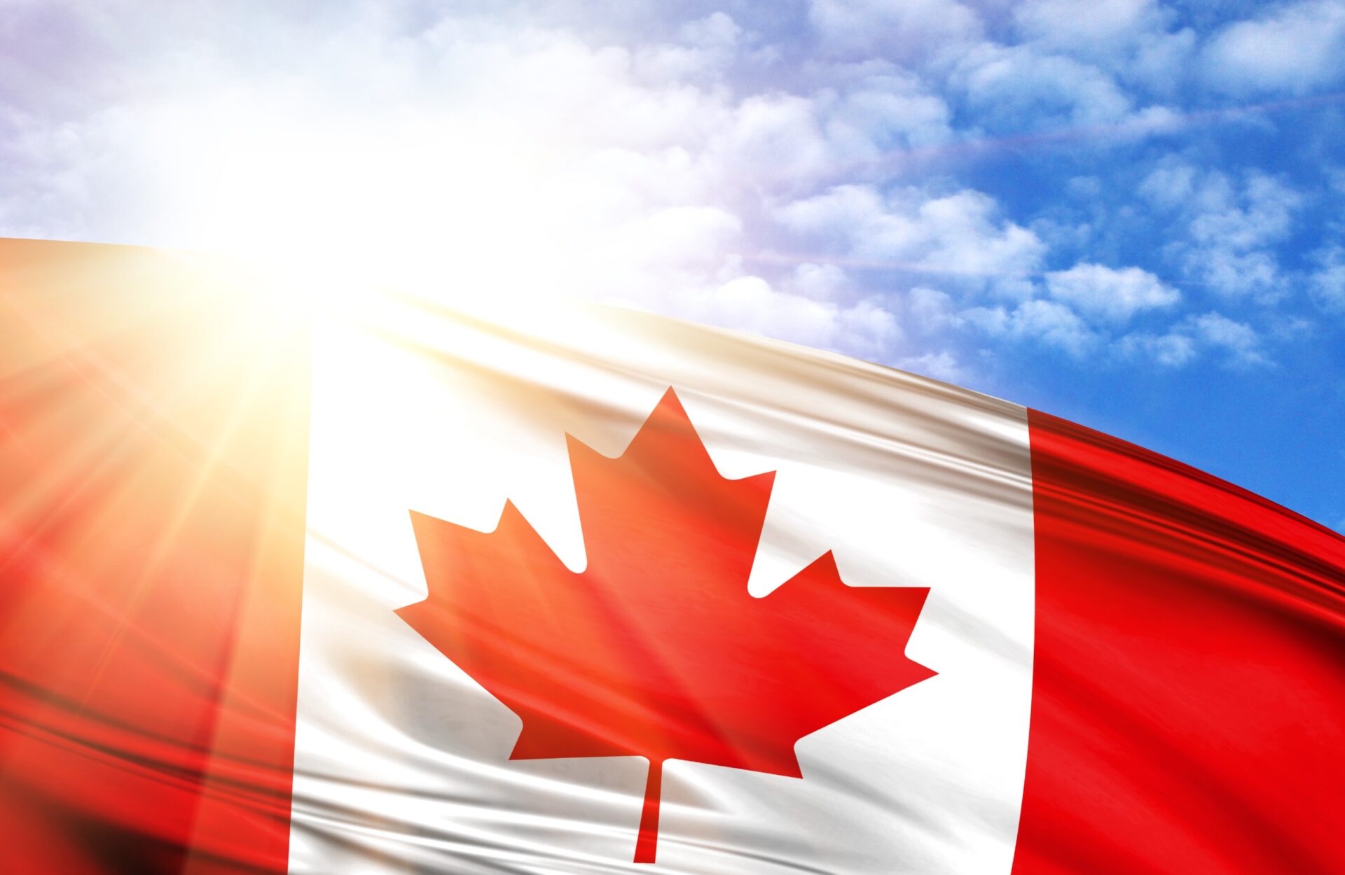 flag of Canada against the blue sky with sun rays.